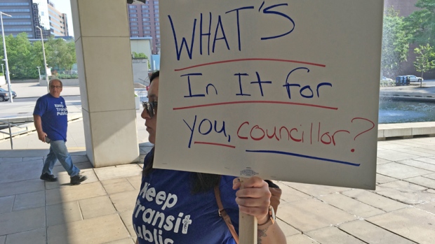 A woman holds up a sign saying, "What's in it for you, councillor?"