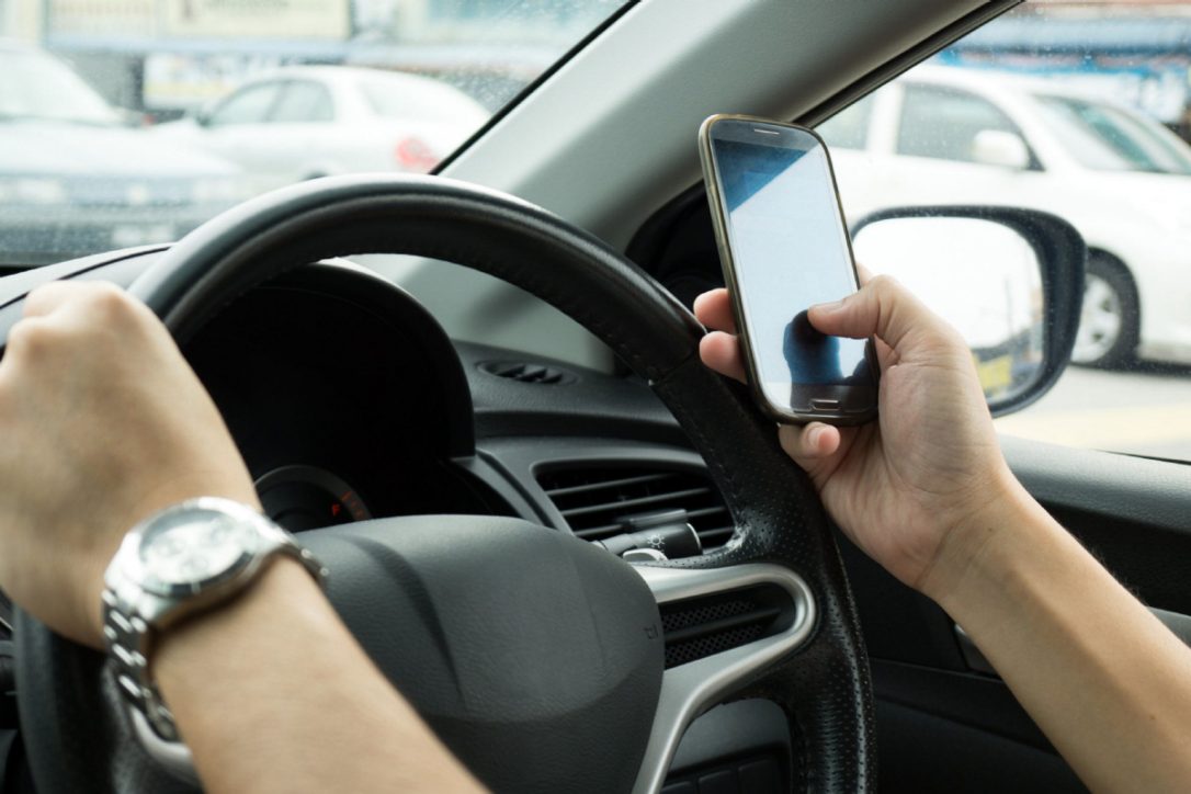 An image of a person using their phone behind the wheel of a vehicle.