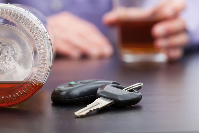 Car keys next to an alcohol bottle, with a half-full glass in the background.