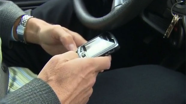 A man is seen texting on a Blackberry phone while sitting behind the wheel of a vehicle.