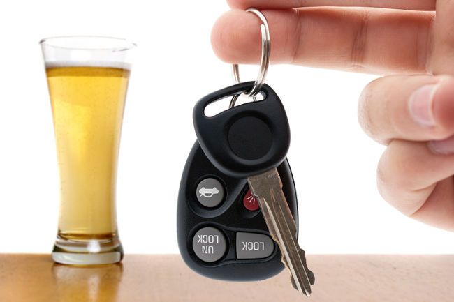 Car keys held in front of a tall glass of alcohol