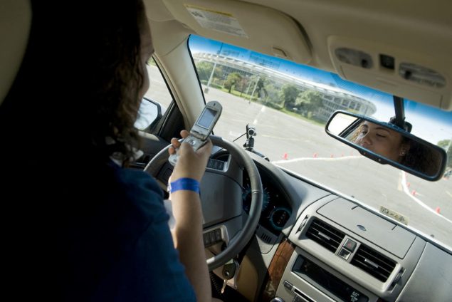 A woman uses a flip phone behind the wheel of a vehicle.