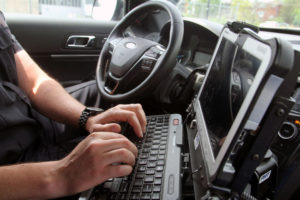 A police officer types on a computer in his car.