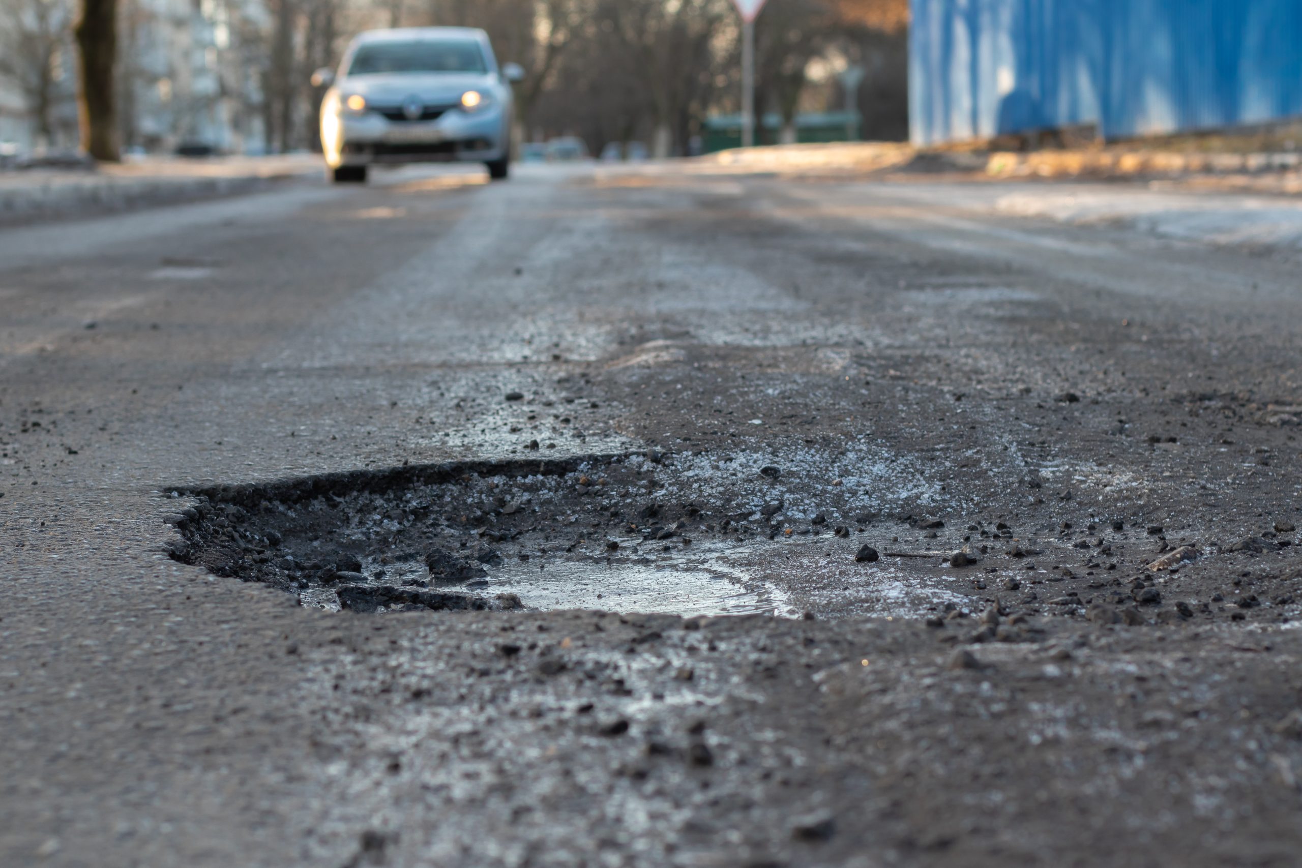 Large pothole in the road with a car approaching 