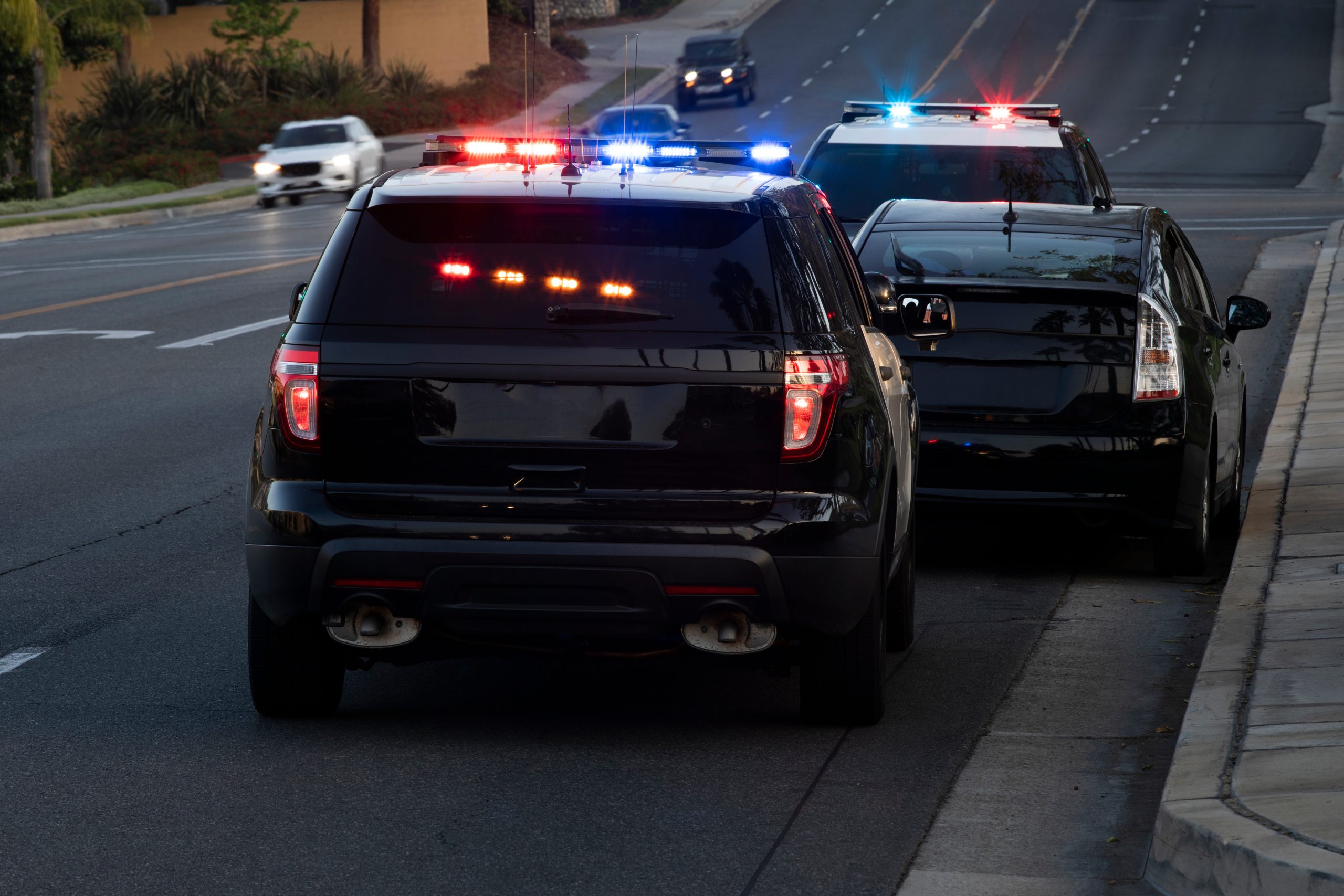 Police vehicles with flashing lights stopped behind a black car on the roadside.