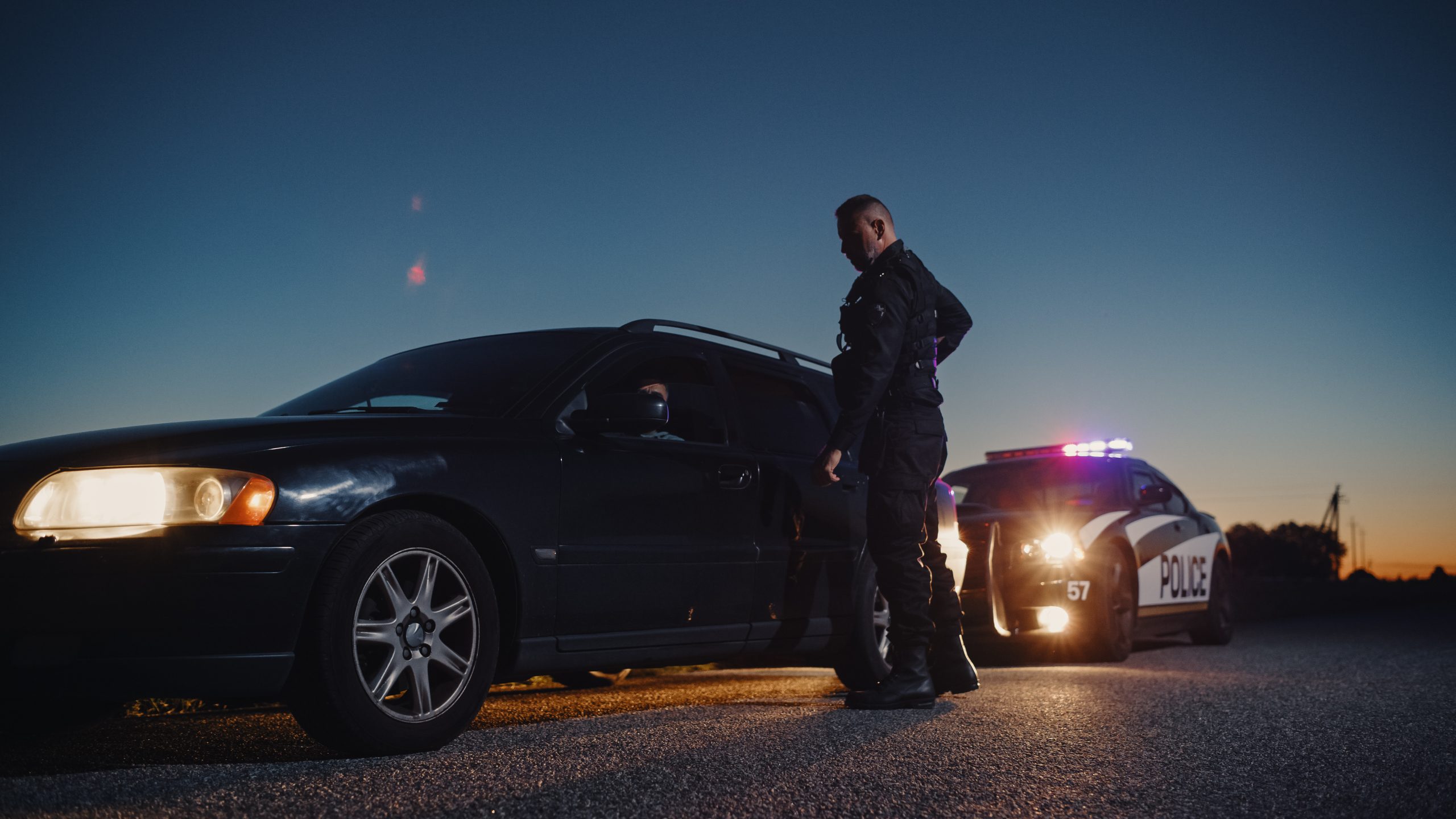 Police officer speaking with a driver during a roadside traffic stop at dusk.
